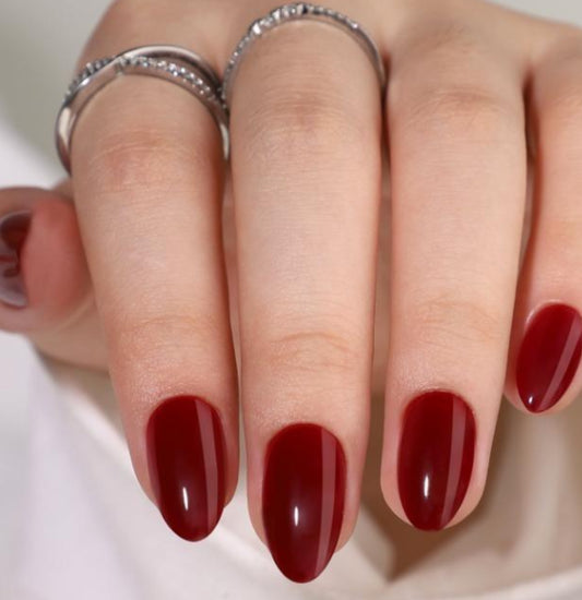 Close-up of a hand with red Red Wine Clawture press on nails on a neutral background