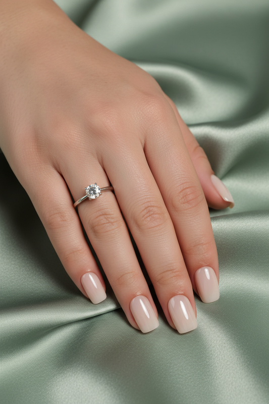 Hand with perla clawture press on false nails wearing a ring with a diamond on a green satin background