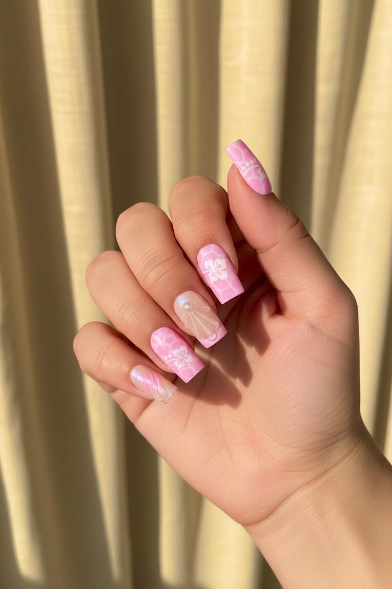 Hand with pink and white glittery Aloha Clawture false press on nails against a beige curtain background
