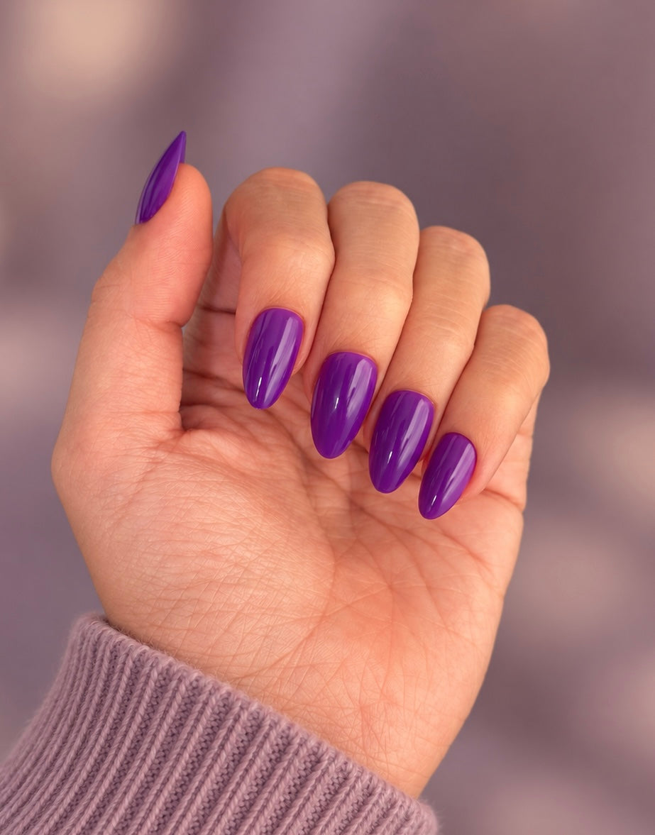 Amethyst Clawture press on nails: hand with glossy almond-shaped vivid purple nails against a soft mauve background with a lilac sweater.
