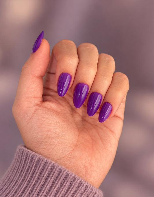 Amethyst Clawture press on nails: hand with glossy almond-shaped vivid purple nails against a soft mauve background with a lilac sweater.