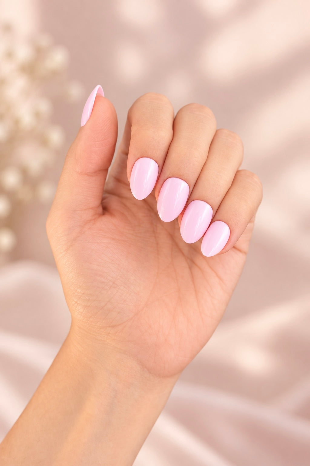 Baby Pink Clawture press on nails: hand with short glossy pastel baby pink almond nails against a soft pink background with dried flowers.