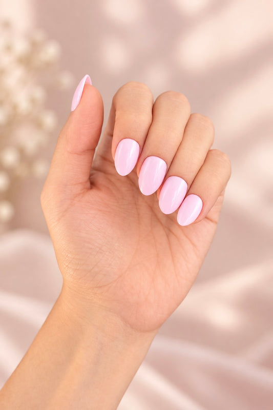 Baby Pink Clawture press on nails: hand with short glossy pastel baby pink almond nails against a soft pink background with dried flowers.