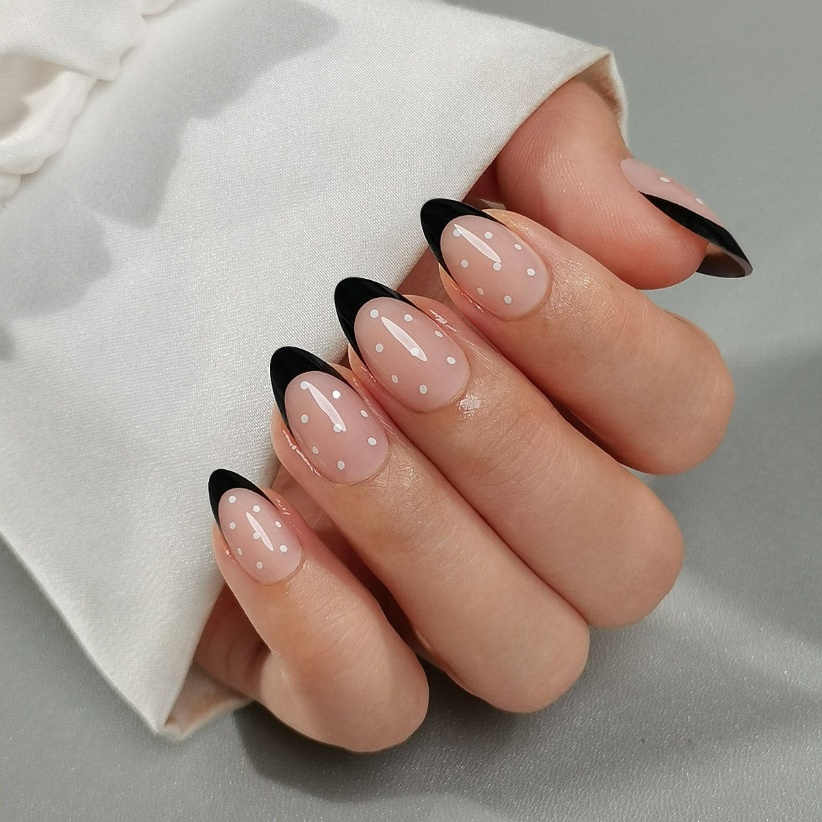 Black & Dotty Clawture press on nails: hand with sheer nude almond nails and bold black French tips on a light background.