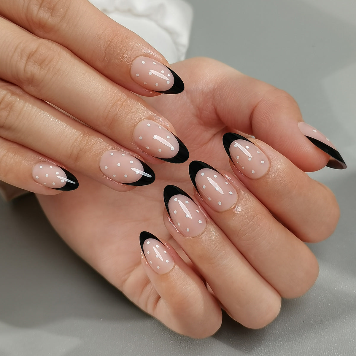 Black & Dotty Clawture press on nails: two hands with almond nude nails and black French tips on a light background.