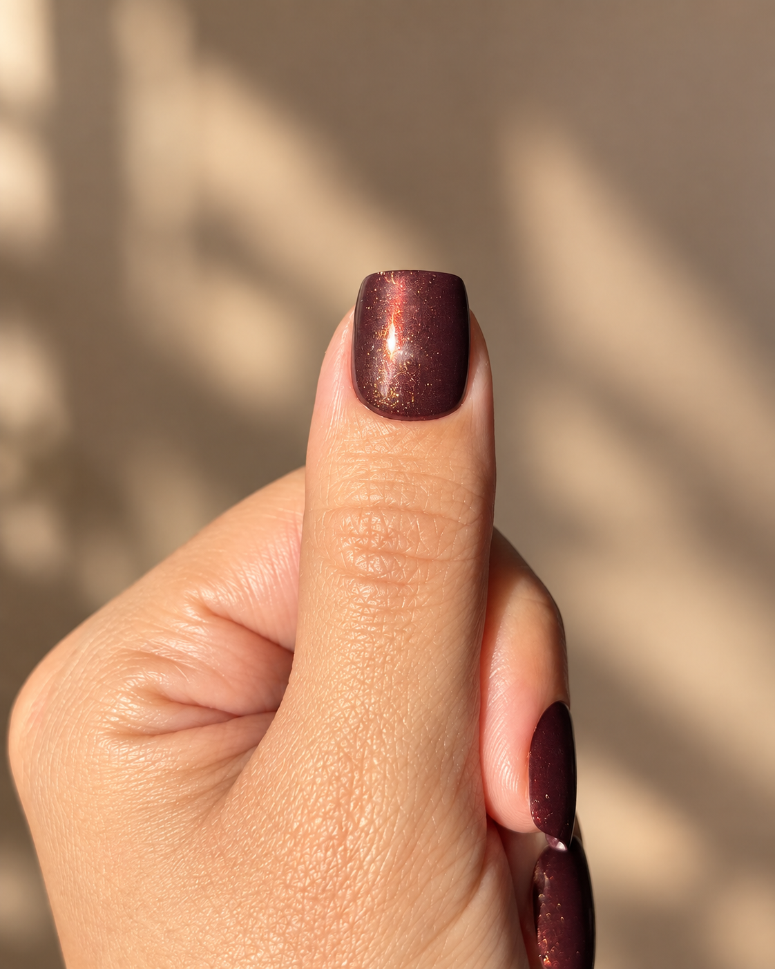 Chocolate Truffle Clawture press on nails: close-up of a thumb with a glossy dark chocolate brown press on nail on a warm background.