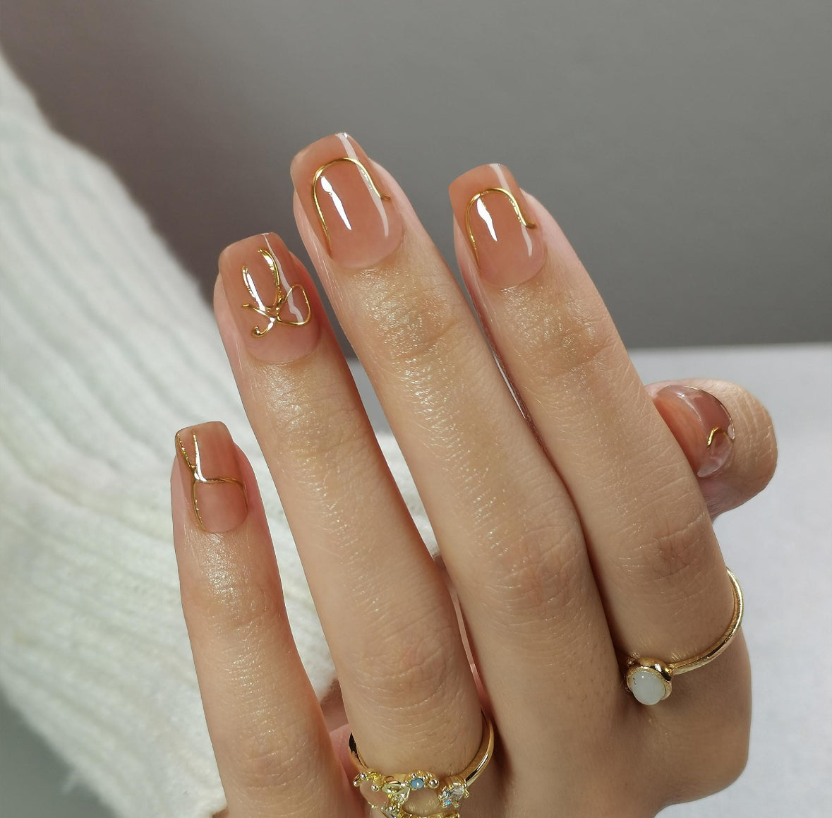 Hand with manicured Clawture Bowtique press on nails with gold nail art on a neutral background