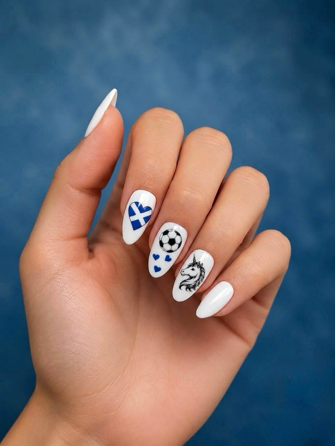 Hand with white nail polish featuring Clawture scotland worldcup football nails designs on a blue background