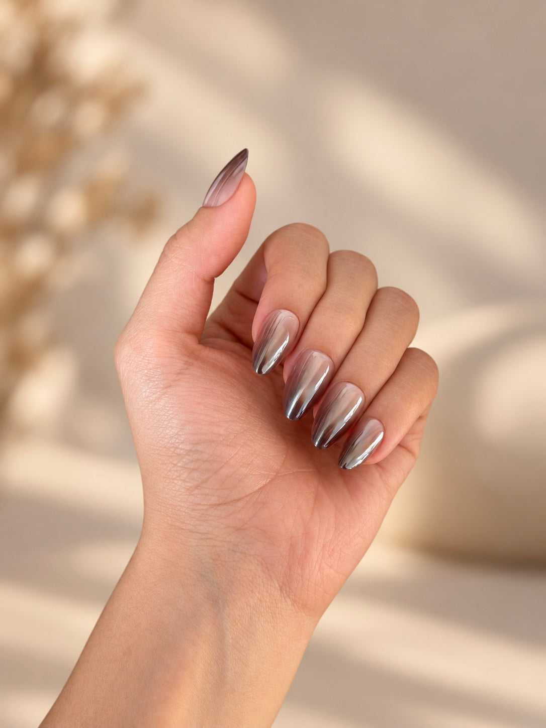 Cocoa Ombré Clawture press on nails: close-up of a hand with long almond-shaped nails in a brown chrome ombré gradient set against a warm beige background with soft shadows.