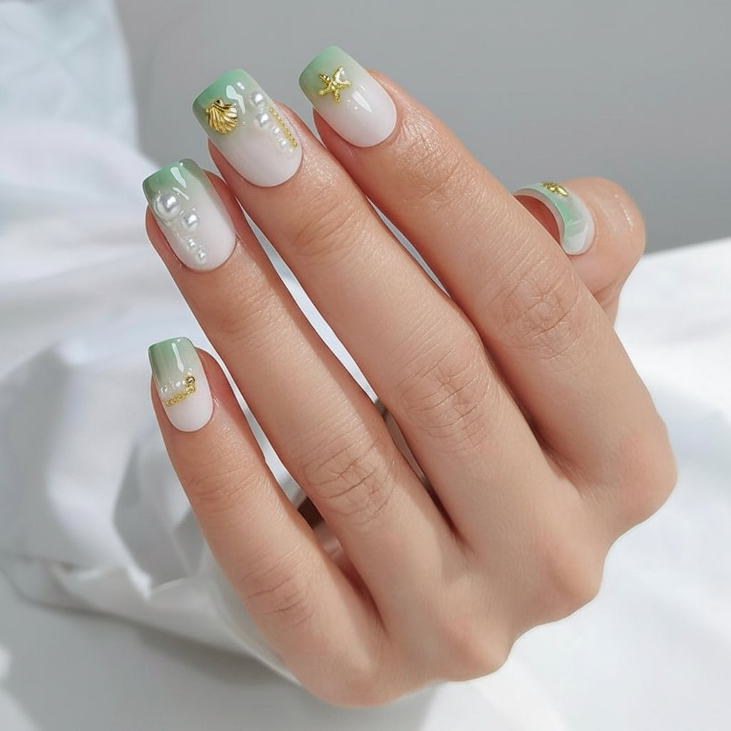 Hand with green and white Hawaii Clawture Press On Nails Sea Ocean Decorations nail polish and gold accents on a neutral background