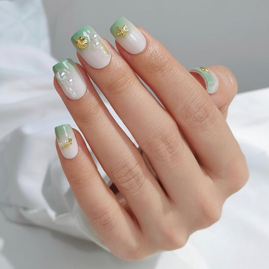 Hand with green and white Hawaii Clawture Press On Nails Sea Ocean Decorations nail polish and gold accents on a neutral background