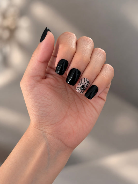 Midnight Butterfly Clawture press on nails: hand with short glossy black nails and butterfly detail on two accent nails on a beige background.