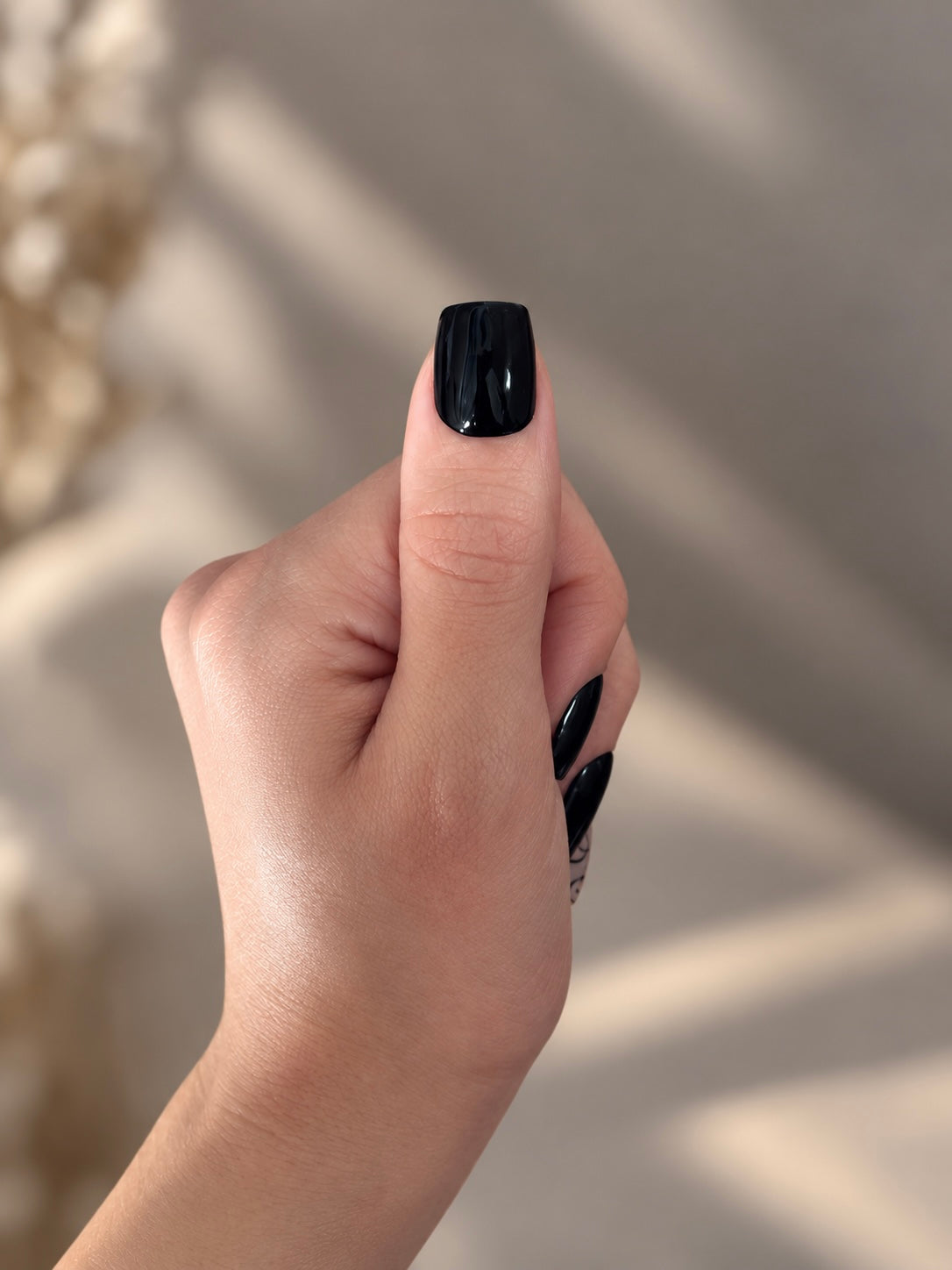 Midnight Butterfly Clawture press on nails: close-up of a thumb with a glossy black press on nail on a soft beige background.