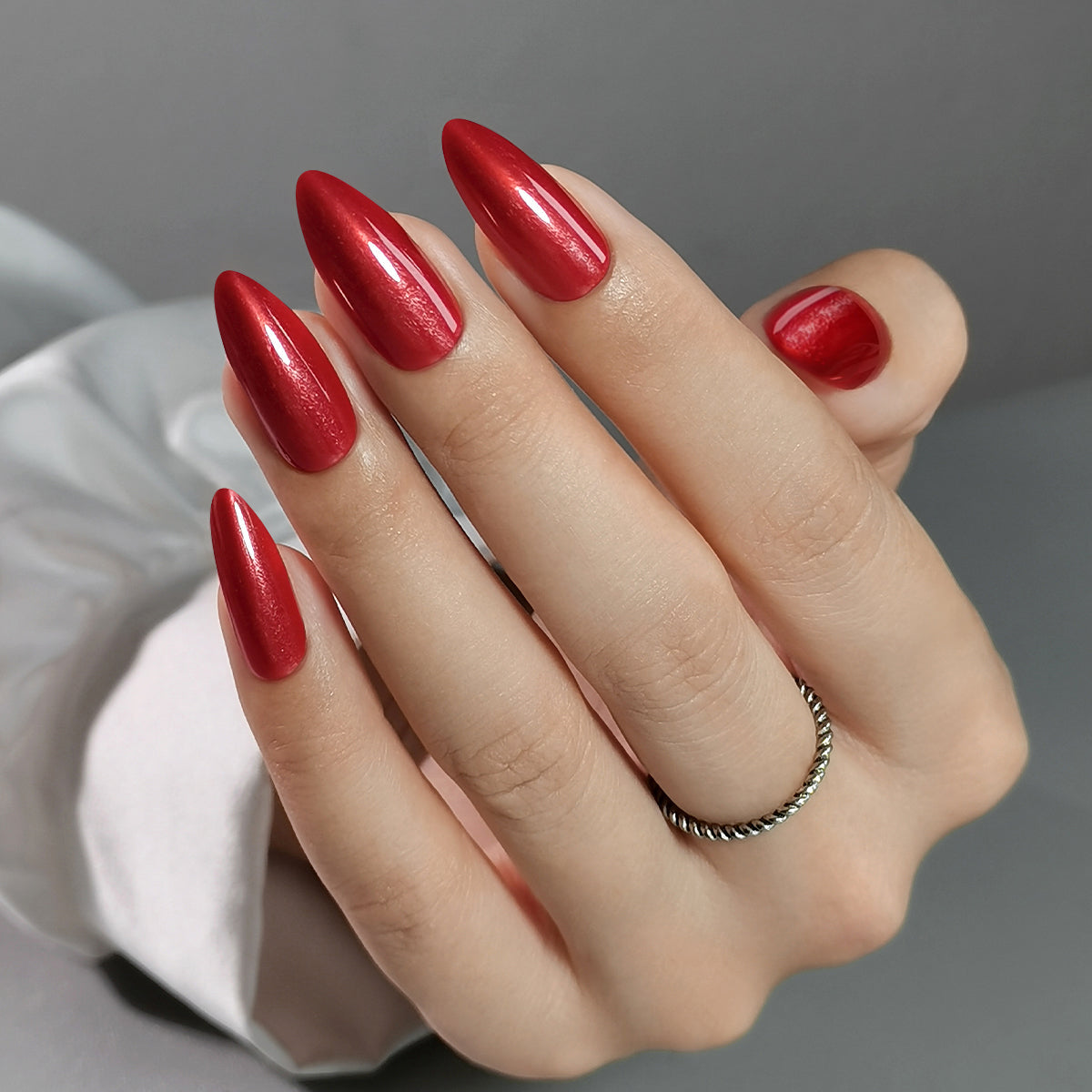 Red Nail Theory Clawture press on nails: hand with long glossy almond-shaped bold red nails on a light grey background.