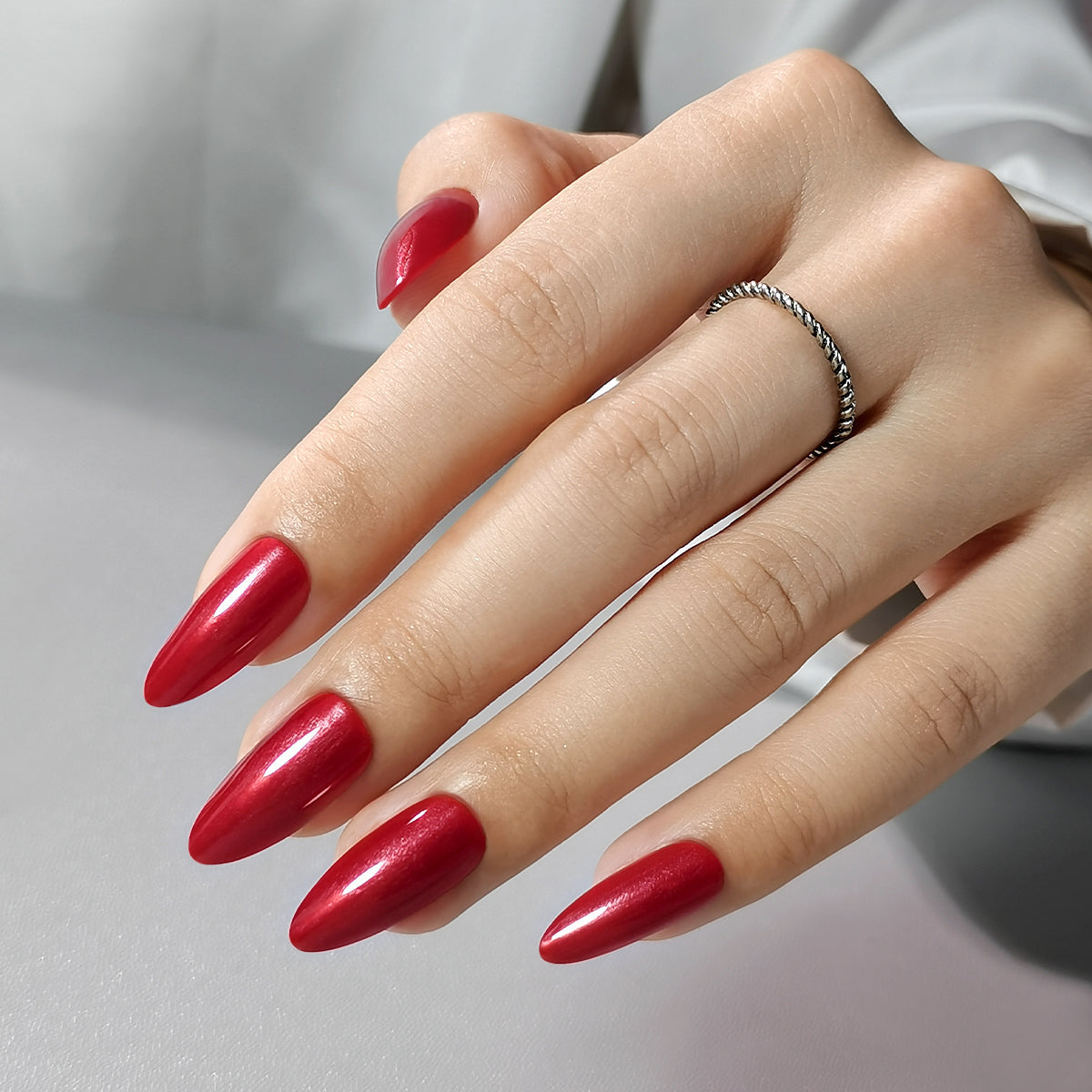 Red Nail Theory Clawture press on nails: hands with long glossy red almond nails and a silver ring on a neutral background.