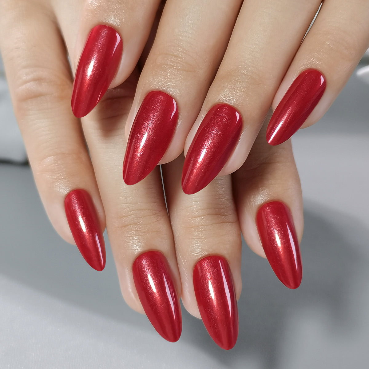 Red Nail Theory Clawture press on nails: close-up of two hands with long pointed almond glossy red nails.