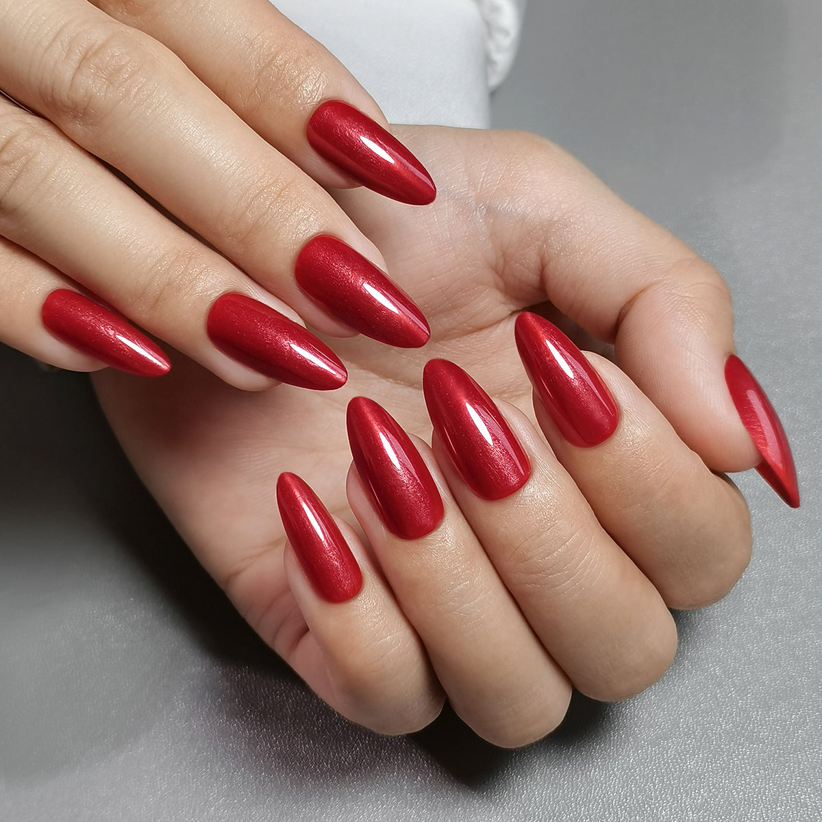 Red Nail Theory Clawture press on nails: hands held together with long glossy red almond nails on a light background.