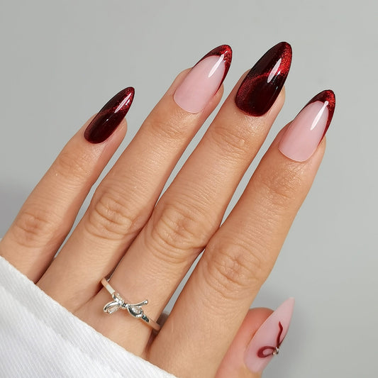 Hand with cherry spell clawture press on false nails maroon and pink nail design on a gray background