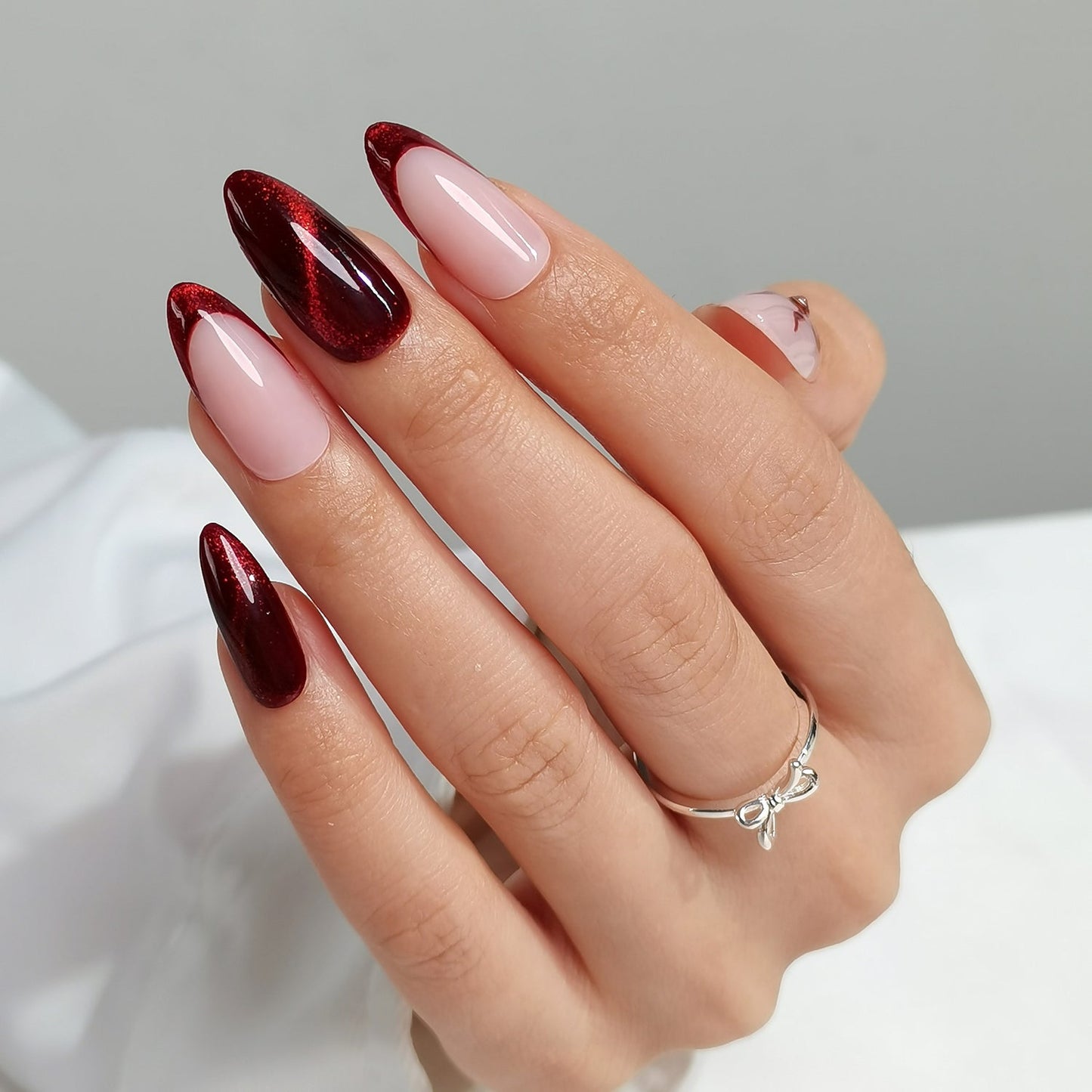 Hand with cherry spell clawture press on false nails maroon and pink nail polish on a neutral background