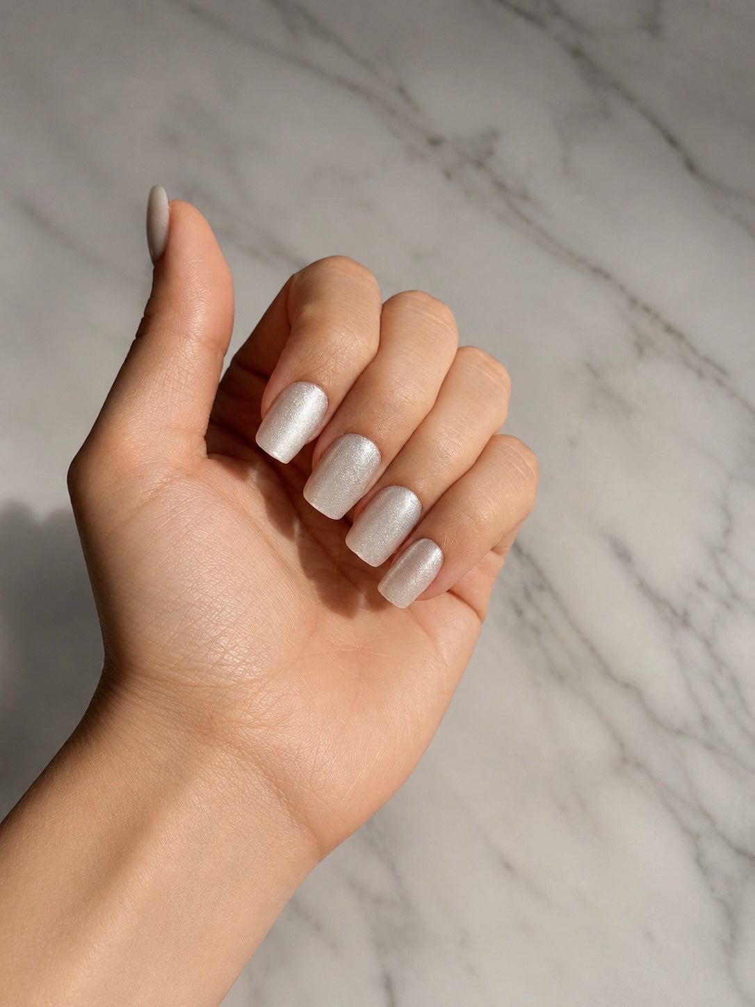 Hand with  clawture angel aura silver cat eye press on nails against a marble background