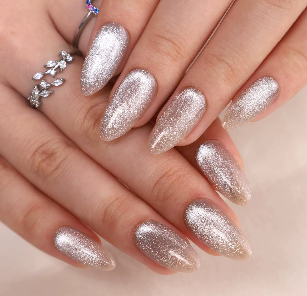Close-up of a hand with glittery silver nails on a neutral background clawture cloud dust press on nails 