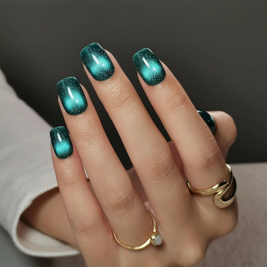 Hand with teal glittery cat eye nail magnetiq clawture press on nails wearing gold rings on a dark background