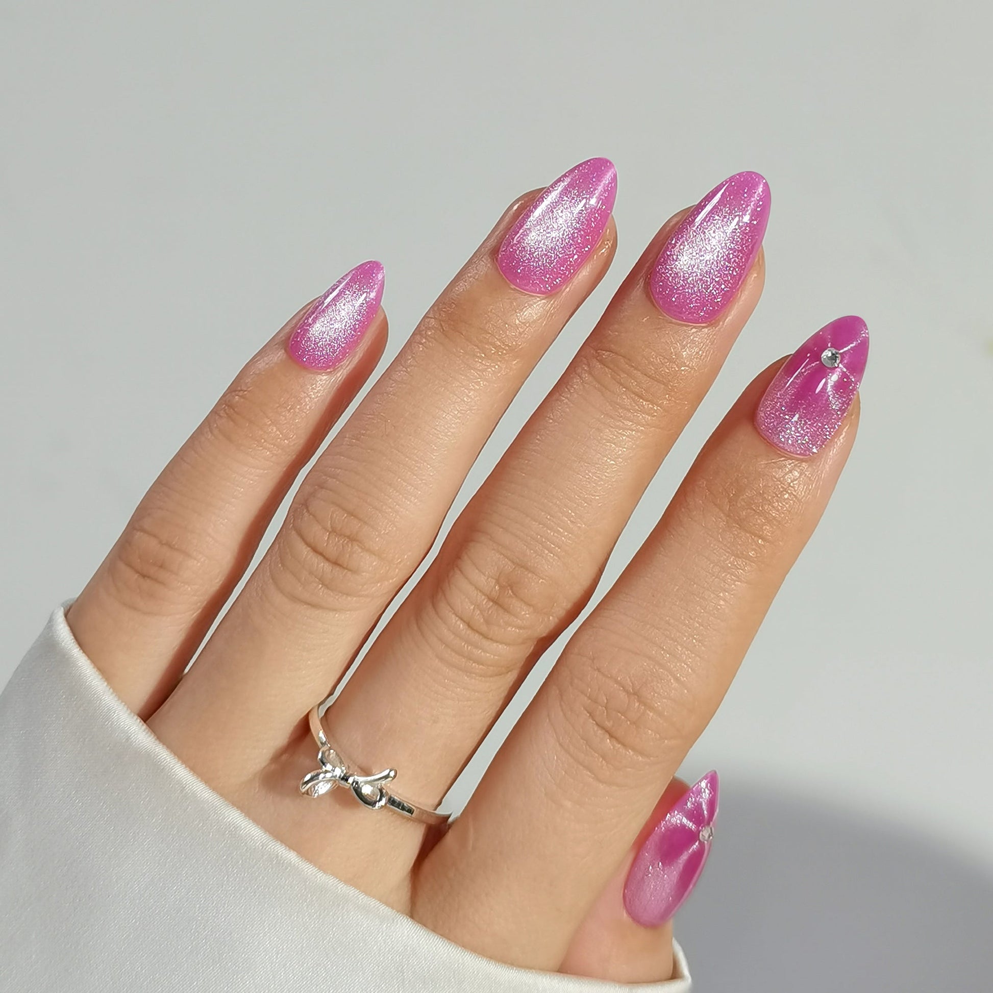 Hand with pink flowertine clawture press on false glittery nails wearing a silver ring on a neutral background