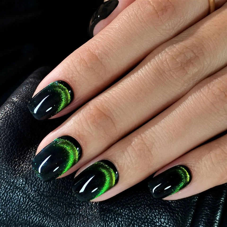 Hand with black and green cat eye effect hidden emerald clawture press on nails on a dark background