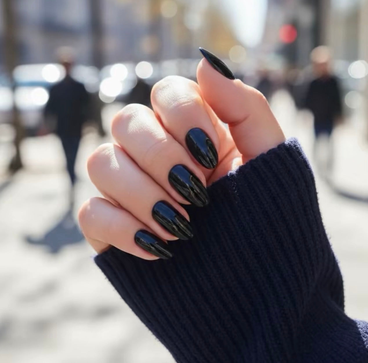 Hand with black noche clawture press on nails wearing a dark blue sleeve against a blurred city street background