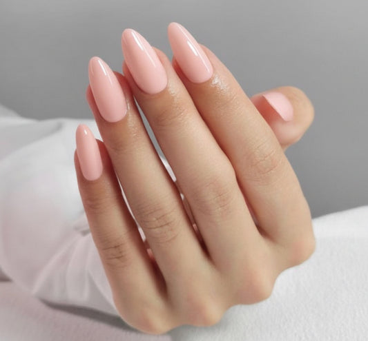 Hand with nude glam clawture press on nails pink nail polish and a gold ring on a neutral background